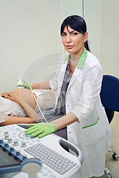 Gynecologist looking at camera during doing ultrasound examination of woman