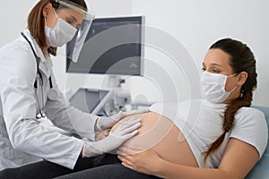 Gynecologist in mask doing palpation of pregnant woman photo