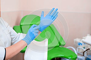 Gynecologist puts on gloves on the background of a gynecological chair. Medical examination