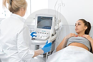 A gynecologist sets up an ultrasound machine to diagnose a patient who is lying on a couch. A transvaginal ultrasound scanner of