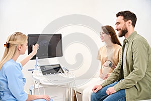 Gynecologist showing ultrasound scanning of woman pregnant belly to couple