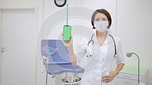 gynecologist shows an smartphone with a chromakey. The doctor in gynecological office shows mobile phone with green