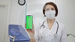 Gynecologist shows an smartphone with a chromakey. The doctor in gynecological office shows mobile phone with green