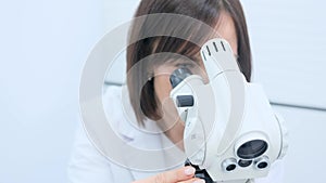 A gynecologist woman looks into a microscope taking a close-up.