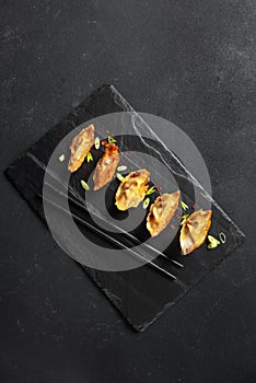 Gyoza or Jiaozi Asian fried dumplings with soy sauce, and green onions on a background of black concrete, top view