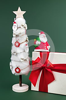 Gypsum colorful santa claus on the gift box and christmas tree with decorations over green background.