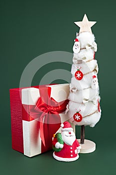 Gypsum colorful santa claus on the gift box and christmas tree with decorations over green background. Copy space