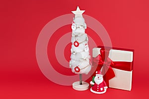 Gypsum colorful santa claus on the gift box and christmas tree with decorations over red background.