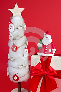 Gypsum colorful santa claus on the gift box and christmas tree with decorations over red background.