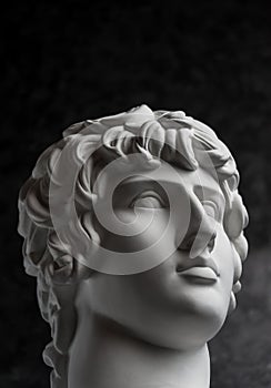 Gypsum copy of ancient statue Antinous head on dark textured background. Plaster sculpture man face. photo