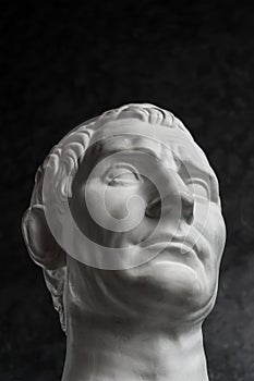 Gypsum copy of ancient statue Augustus head on dark textured background. Plaster sculpture man face.