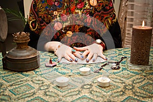 Gypsy fortune girl stands near the table with magical attributes: candles, cards, bahurs and etc