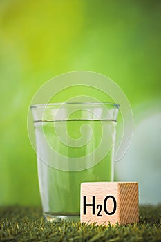 h2o water, Impact of water on the environment, Environmental science concept, Glass of water on green background, wooden block
