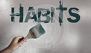 Habits Sign Painted and a hand holding paintbrush on light grey wall background. Bad habits addiction concept