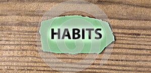 HABITS - word on green torn piece of paper on old brown board background