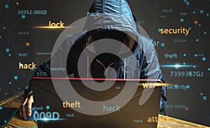 A hacker anonymous in a hood is typing on a laptop keyboard in a dark room. Cybercrime fraud and identity theft