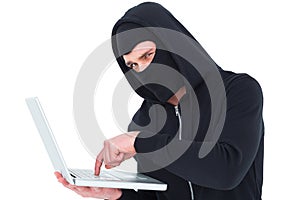 Hacker in balaclava typing on laptop