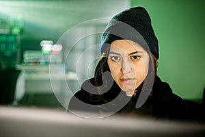 Female young hacker working on computer in dark room programming code