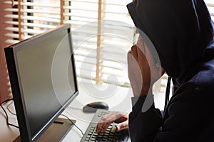 A hacker in a hooded sweatshirt with a hidden face typing on a computer keyboard and talking on a mobile phone.
