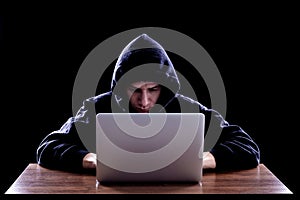 Hacker in a dark hoody sitting in front of a notebook