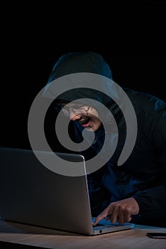 Hacker in a dark hoody sitting in front of a notebook. Computer
