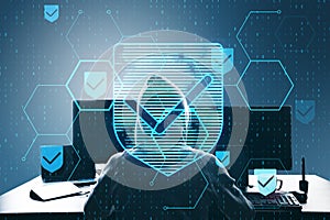 Hacker at desktop using laptop with glowing hexagonal shield hologram with binary coding on blurry background. Safety, hacking,