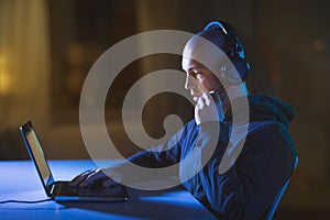 Hacker in headset typing on laptop in dark room