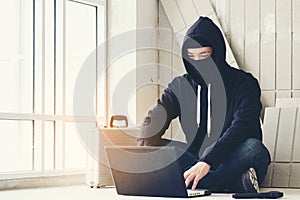 Hacker holding gun working on his computer, war, terrorism , terrorist and bandit concept. Glitch effect and copy space. Black ma