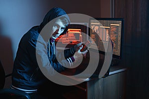 Hacker in the hood holding the phone in his hands trying to hack the mobile device cloud in neon light. Cyber security