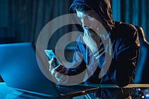 Hacker in the hood holding the phone in his hands trying to steal access databases with passwords. Cybersecurity