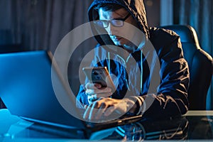 Hacker in the hood holding the phone in his hands trying to steal access databases with passwords. Cybersecurity
