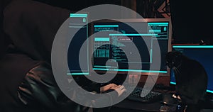Hacker in a hood sits in front of computer screens and hacks databases