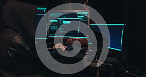 Hacker in a hood sits in front of computer screens and hacks databases