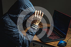 Hacker in a hood is typing on a laptop keyboard in a dark room. Concept of cyber warfare and Dos attacks