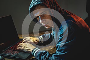 Hacker in a hood is typing on a laptop keyboard in a dark room. Concept of cyber warfare and Dos attacks