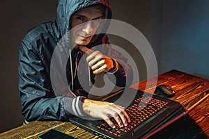 Hacker in a hood is typing on a laptop keyboard in a dark room. Cybercrime fraud and identity theft