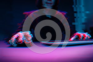 Hacker in the hood working with computer typing text in dark room. Image with glitch effect