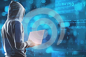 Hacker in hoodie using laptop with abstract glowing blue coding background. Binary code, theft, technology, data and internet