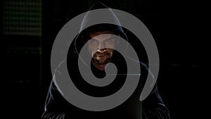 Hacker in hoodie using laptop and looking into camera with evil eyes, malware