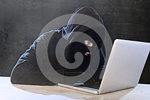 Hacker man in black hood and mask with computer laptop hacking system in digital intruder cyber crime concept photo