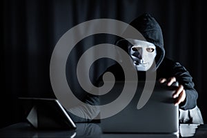 Hacker man holding white mask looking at laptop