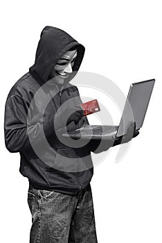 Hacker man wearing anonymous mask holding laptop and credit card