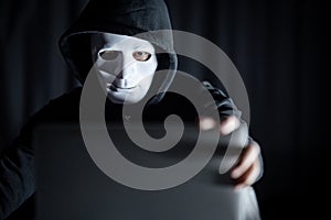 Hacker man in white mask holding laptop