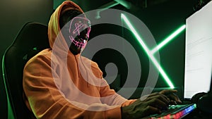 hacker in an orange hood and with a mask hacking databases medium shot cyberterrorism concept indoors