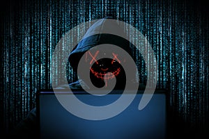 Hacker with red glowing mask behind notebook laptop in front of blue source binary code background internet cyber hack attack