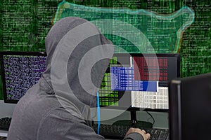 A hacker sits behind computer monitors on an abstract background, attacking and hacking servers with a virus. Creation and dissemi