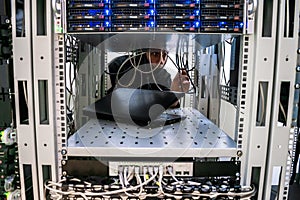 Hacker switches the wires in the server room. The malefactor is behind the computer equipment of the data center. A man in a mask photo