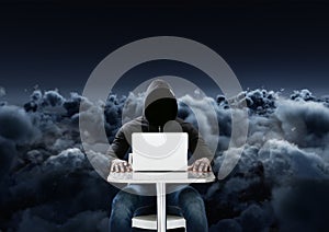 Hacker using a laptop in front of cloudy black background