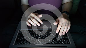 Hacker using laptop. hands typing on PC late at night, view from above. Unrecognizable girl, sitting in a dark room. Bright from