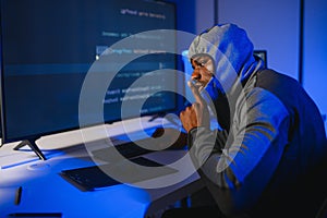 African american Hacker Using Multiple Computers For Stealing Data On Desk